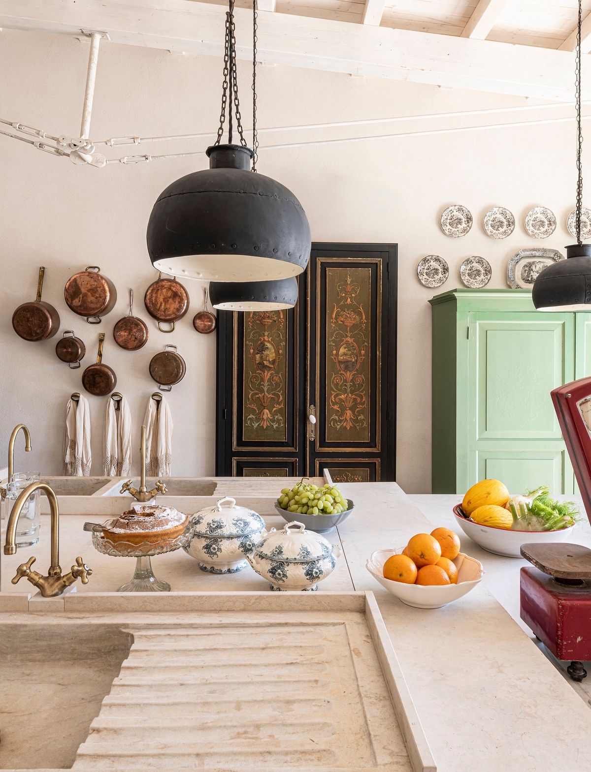 Cucina con lampade in ferro, pentole in rame, zuppiere in ceramica e frutta di stagione